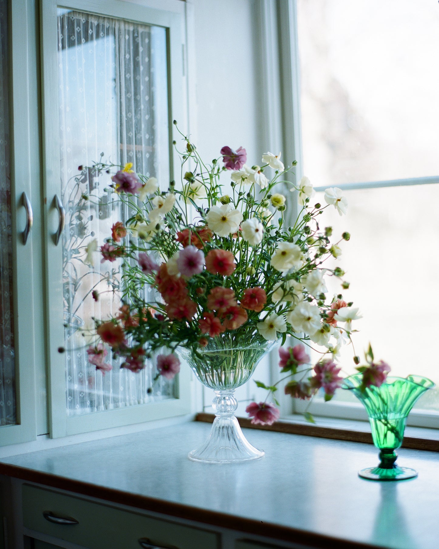 Large mouth blown clear Murano vase in window with flowers.