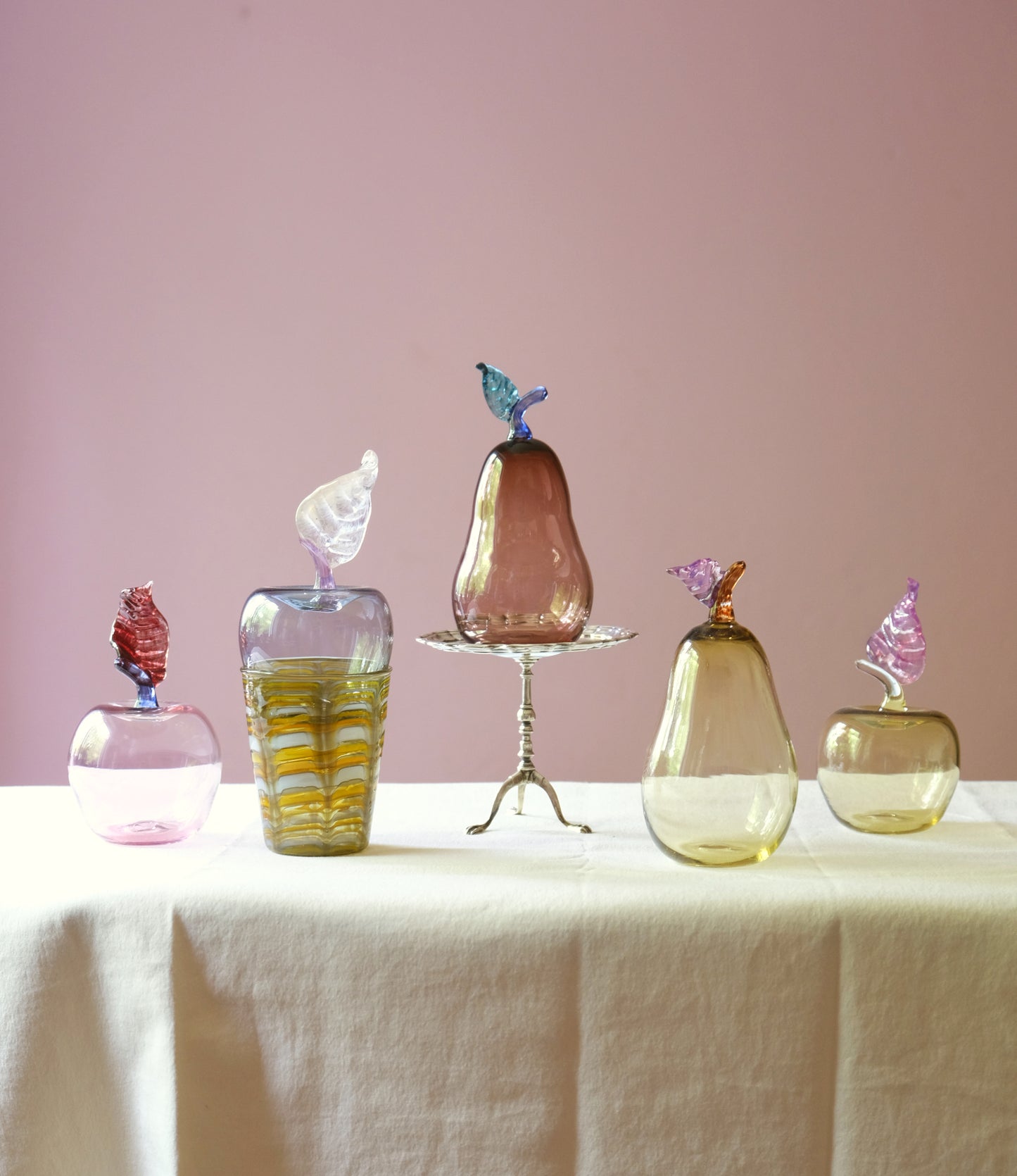 Mouth blown glass paperweights shaped as apples and pears placed on a table.