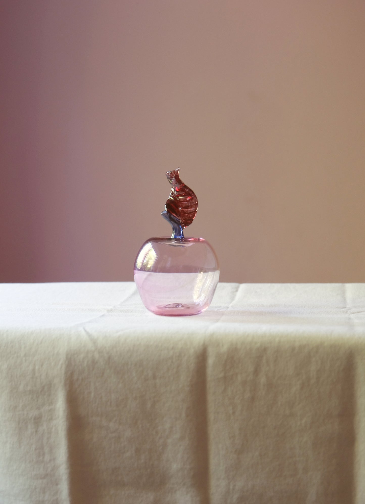 Mouth blown glass paperweight shaped as an apple placed on a table.