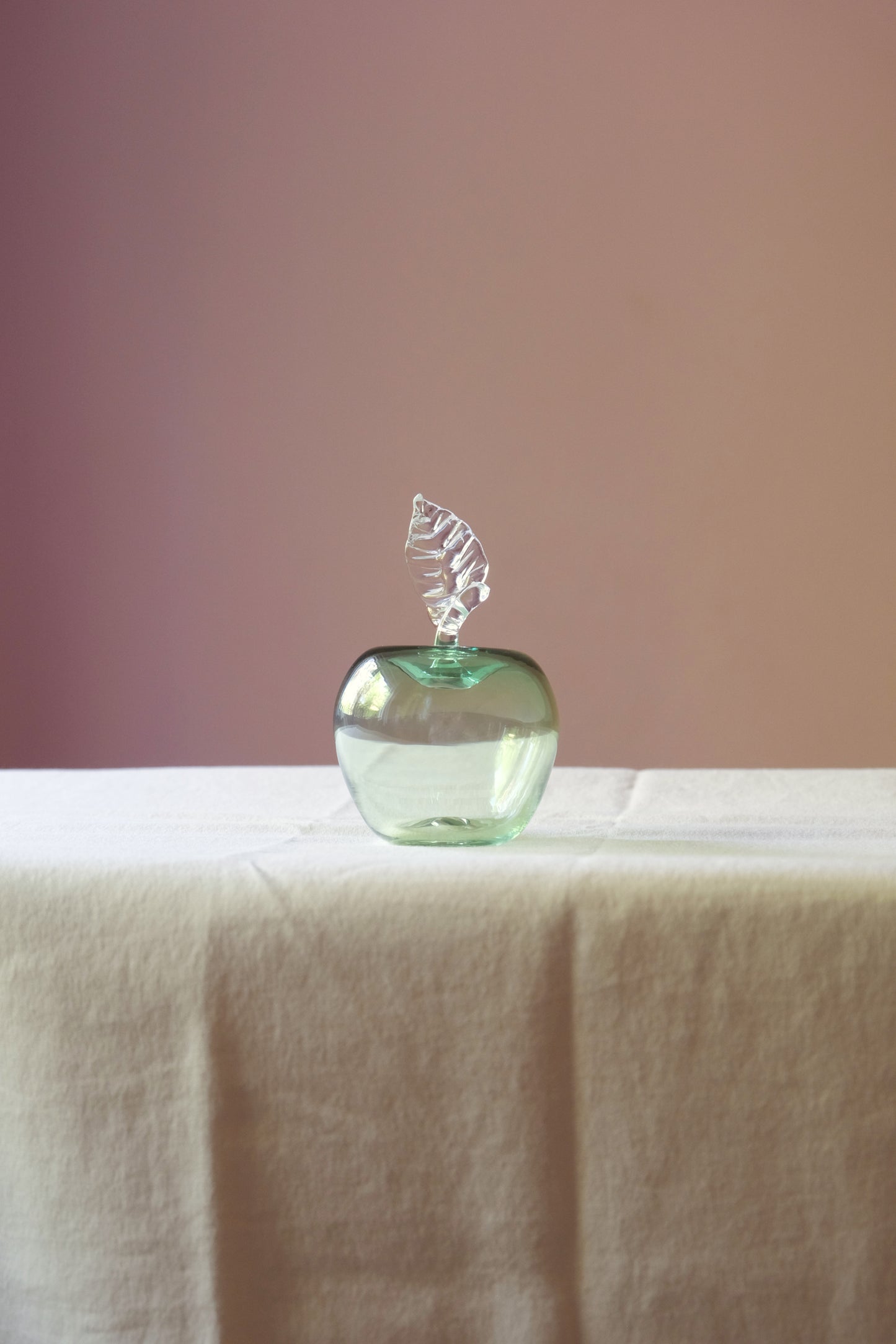 Mouth blown glass paperweight shaped as an apple placed on a table.