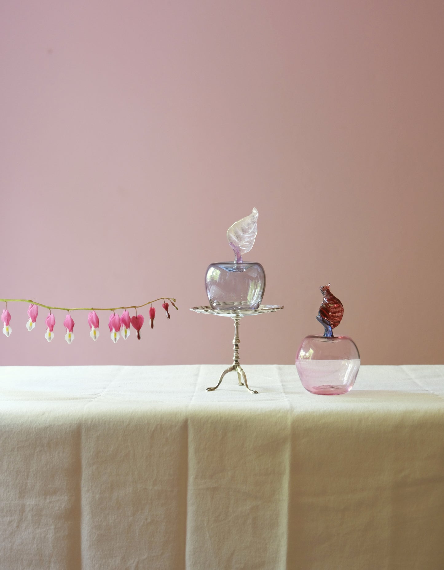 Two mouth blown glass paperweights shaped as applea placed on a table.