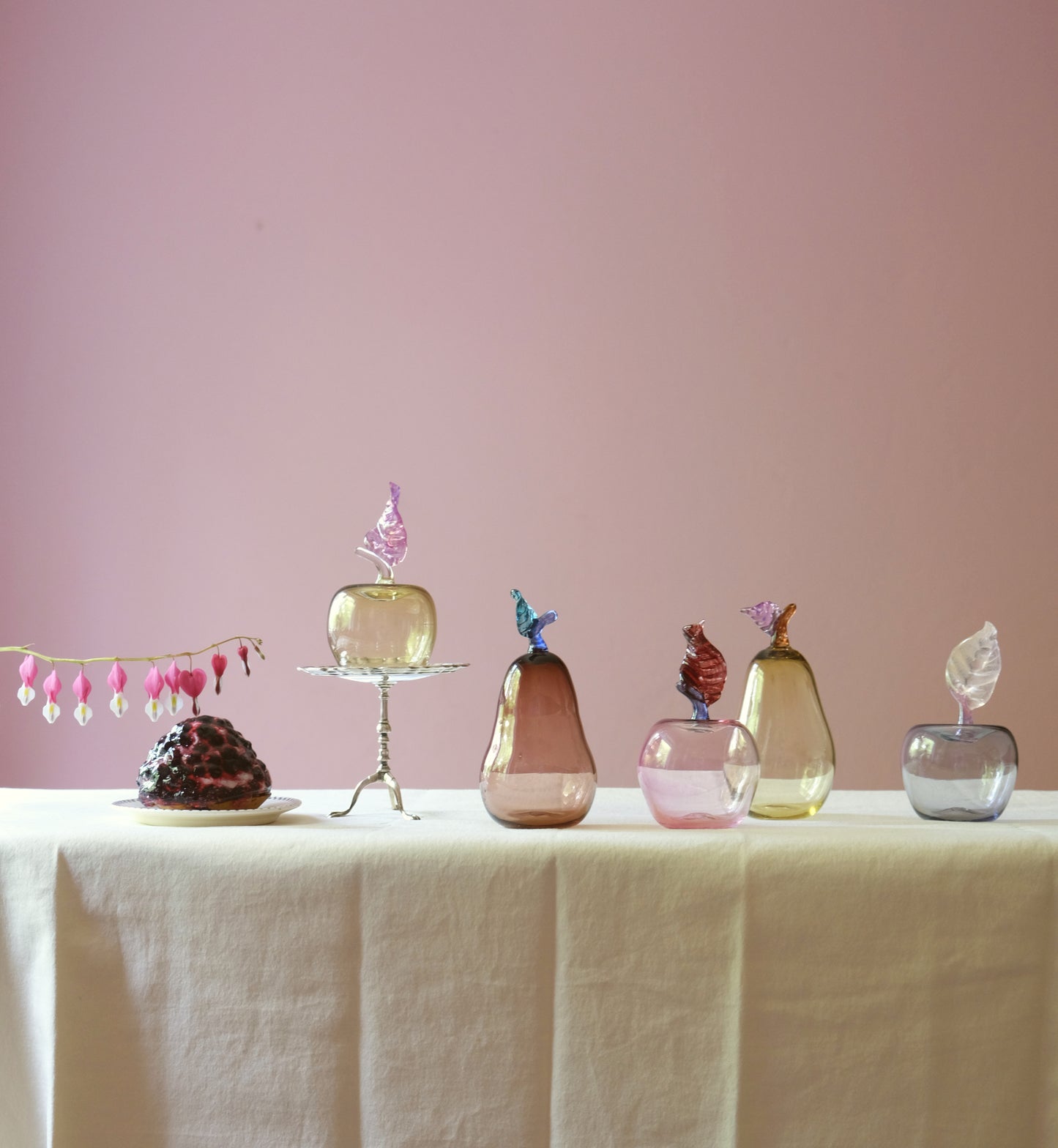 Mouth blown glass paperweight shaped as apples and pears placed on a table.