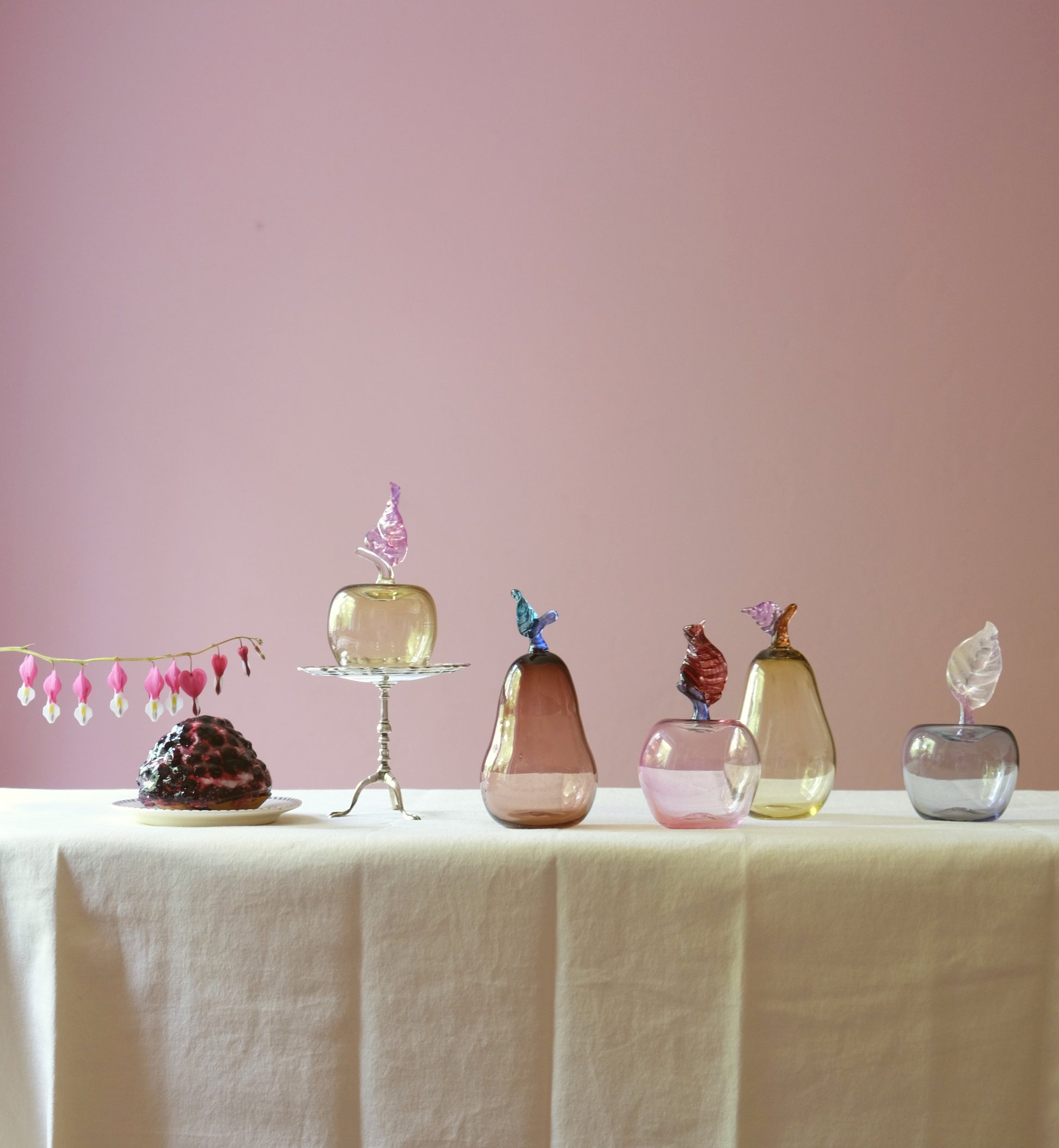 Mouth blown glass paperweight shaped as apples and pears placed on a table.