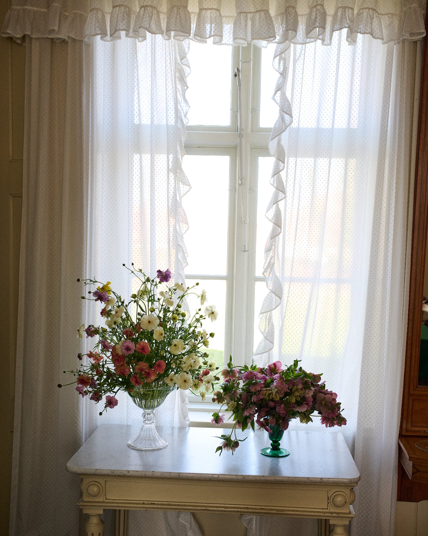Large and small mouth blown clear and green Murano vase in window with flowers.