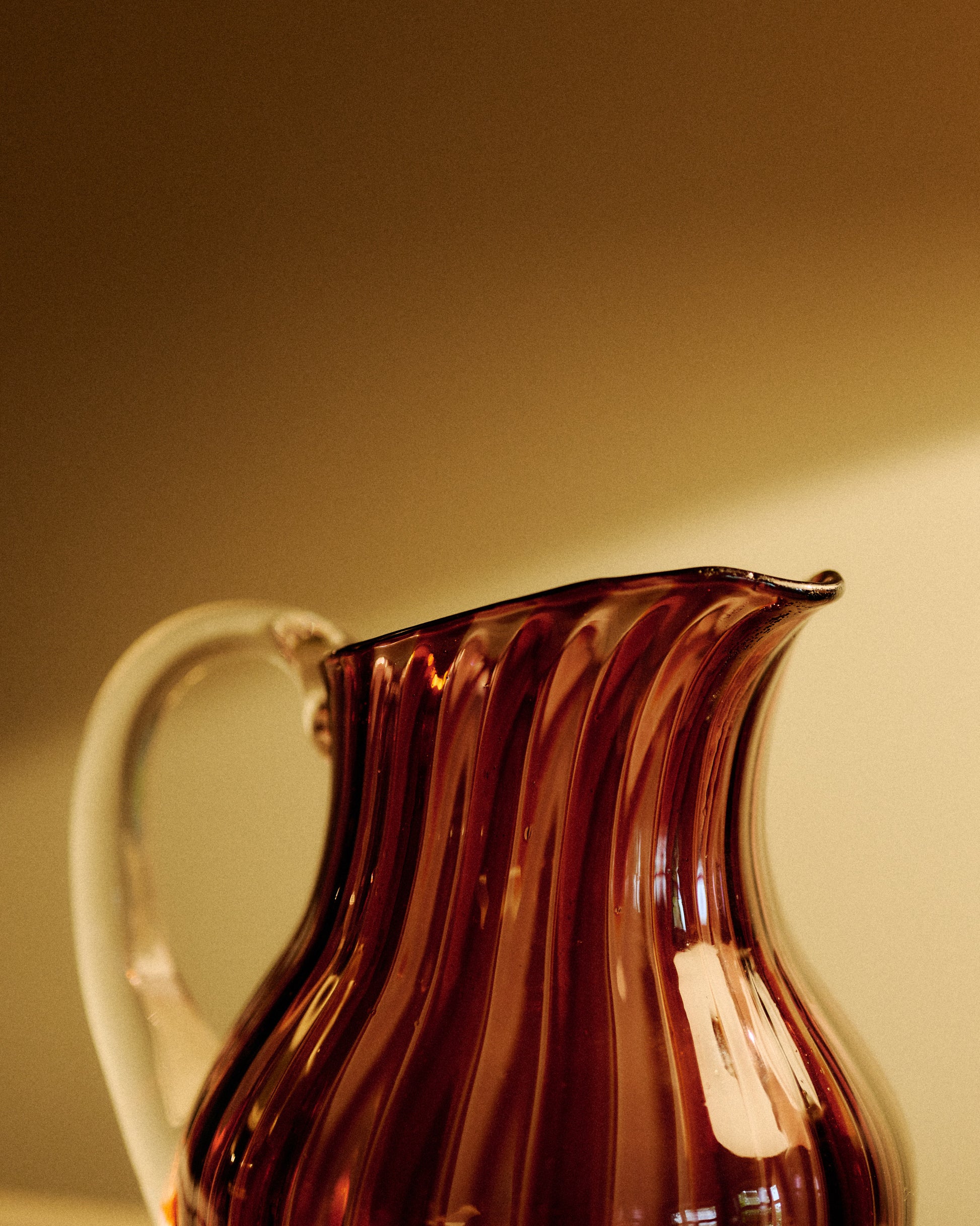 A striped glass pitcher with in amber and pink with a clear handle. 