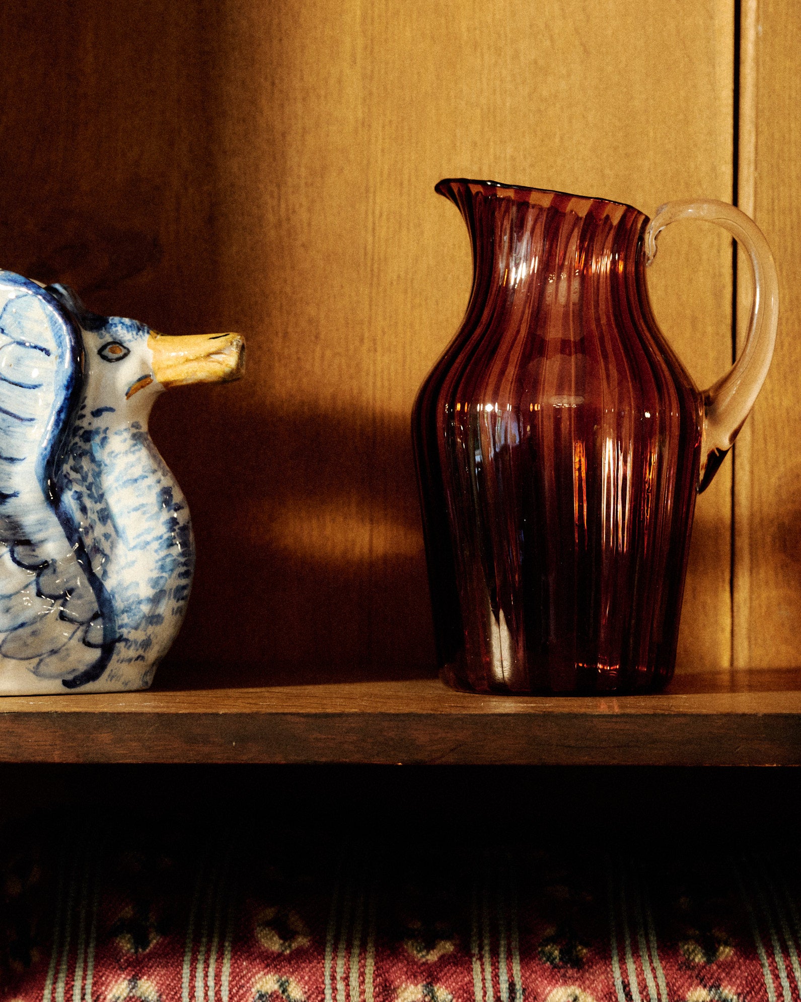 A striped glass pitcher in amber and pink with a clear handle. 