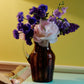 A striped glass pitcher with flowers in amber and pink and a clear handle. 