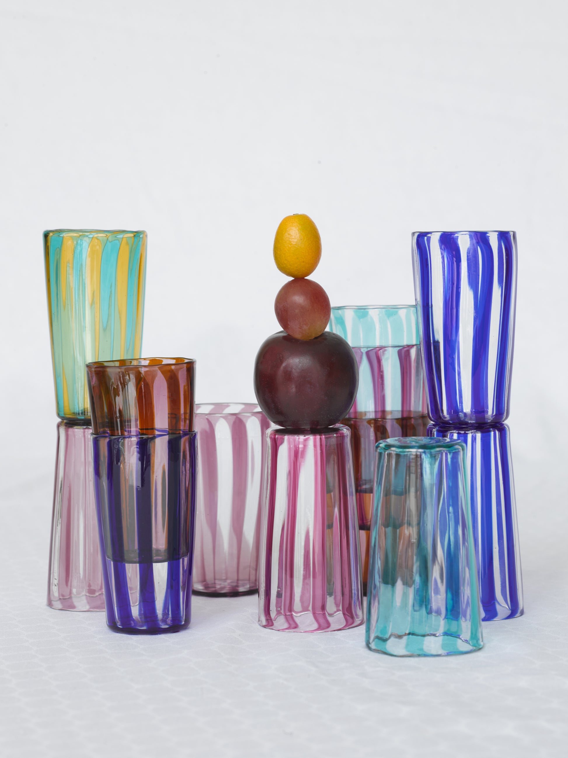 Multiple small striped handmade Murano glasses and fruits in different colors.