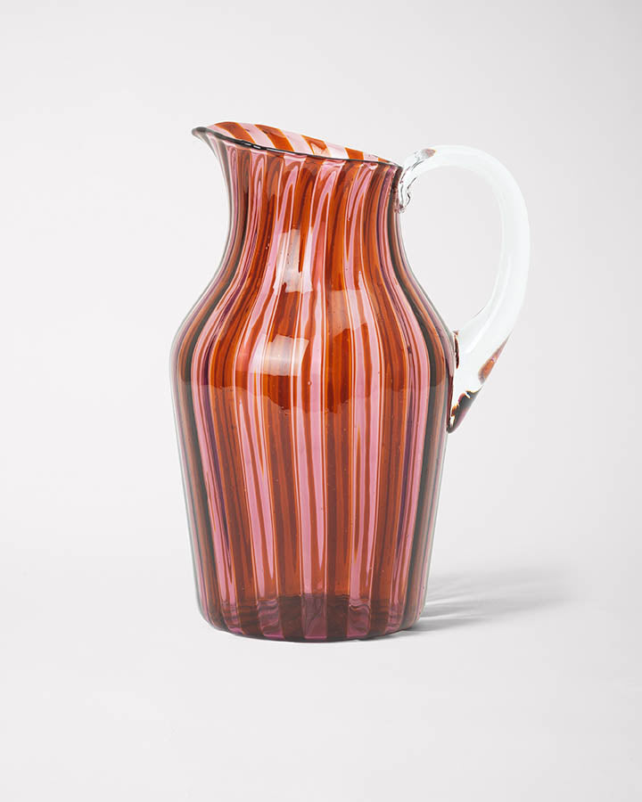 A striped glass pitcher with amber and pink hues and a clear handle.