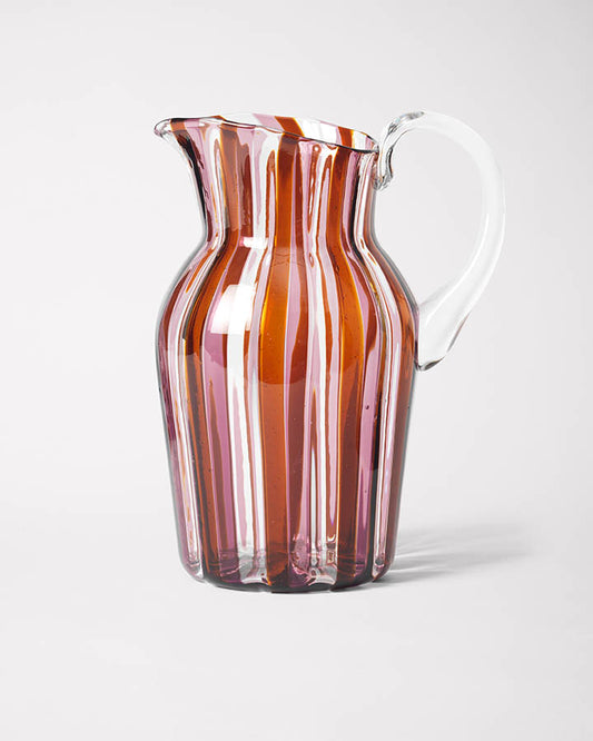 A striped glass pitcher with amber and pink hues and a clear handle.